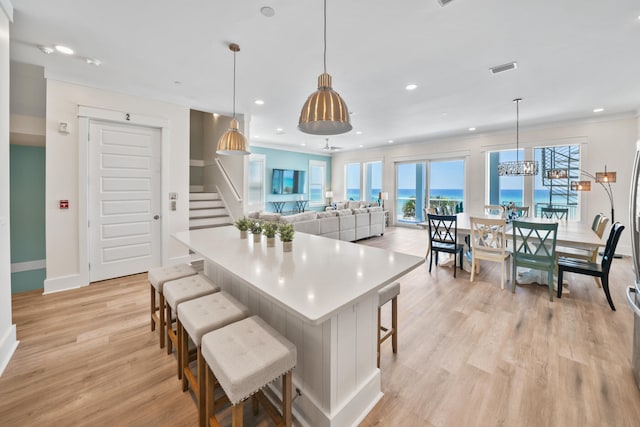 kitchen with a water view, hanging light fixtures, a breakfast bar area, and light wood-type flooring