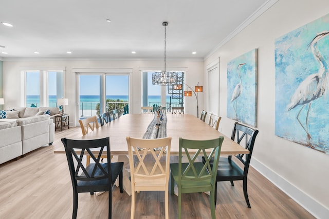 dining space featuring an inviting chandelier, light hardwood / wood-style flooring, crown molding, and a water view