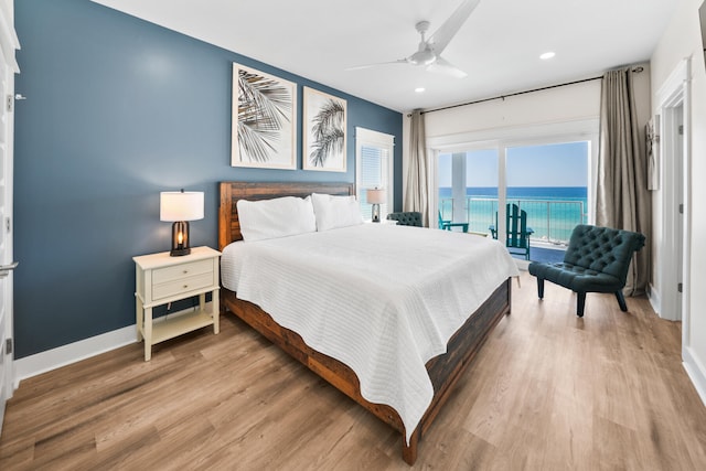 bedroom with wood-type flooring, ceiling fan, a water view, and access to exterior