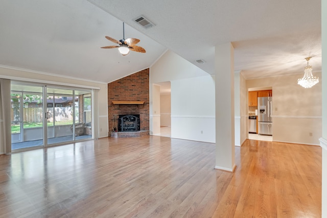 unfurnished living room with light wood-type flooring, ceiling fan with notable chandelier, a brick fireplace, ornamental molding, and brick wall