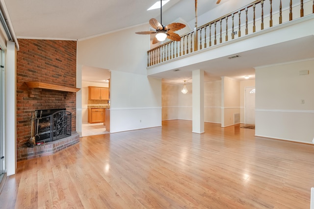 unfurnished living room with high vaulted ceiling, a fireplace, light wood-type flooring, crown molding, and ceiling fan