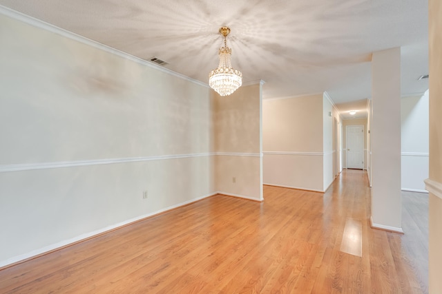 empty room featuring light hardwood / wood-style floors, a chandelier, and crown molding