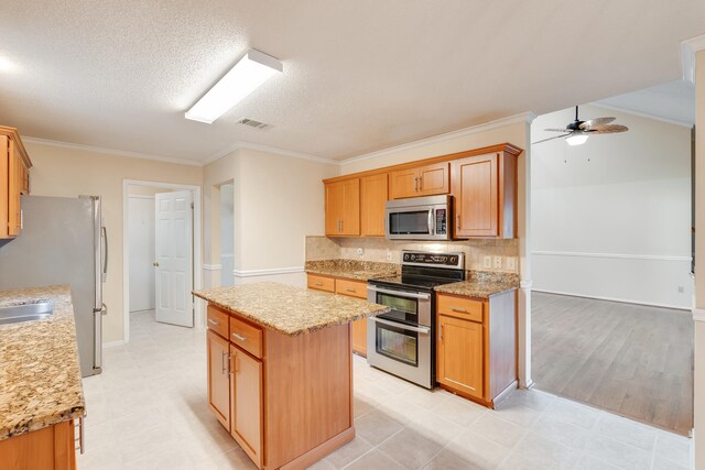 kitchen featuring appliances with stainless steel finishes, a center island, ceiling fan, light tile flooring, and crown molding