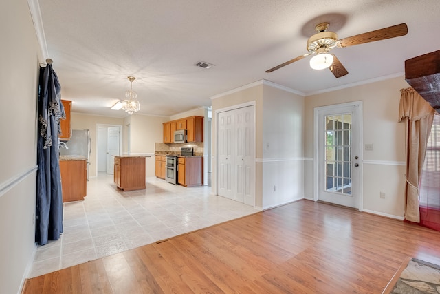 kitchen with appliances with stainless steel finishes, light tile flooring, ceiling fan with notable chandelier, crown molding, and pendant lighting