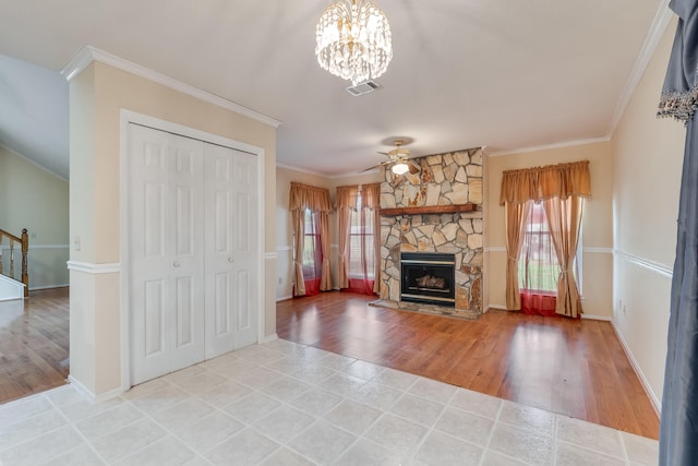 unfurnished living room with ceiling fan with notable chandelier, tile flooring, ornamental molding, and a stone fireplace