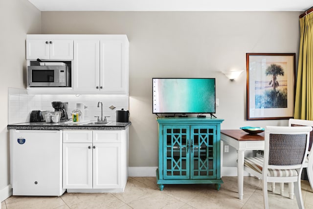 kitchen with backsplash, light tile flooring, stainless steel microwave, and white cabinetry