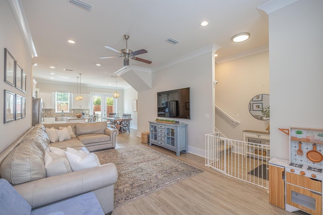 living room featuring crown molding, baseboards, visible vents, and light wood-style floors