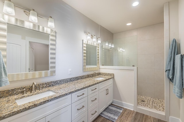 bathroom featuring double vanity, a walk in shower, a sink, and wood finished floors