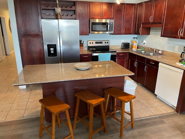 kitchen featuring appliances with stainless steel finishes, a center island, light tile floors, a breakfast bar area, and light stone countertops