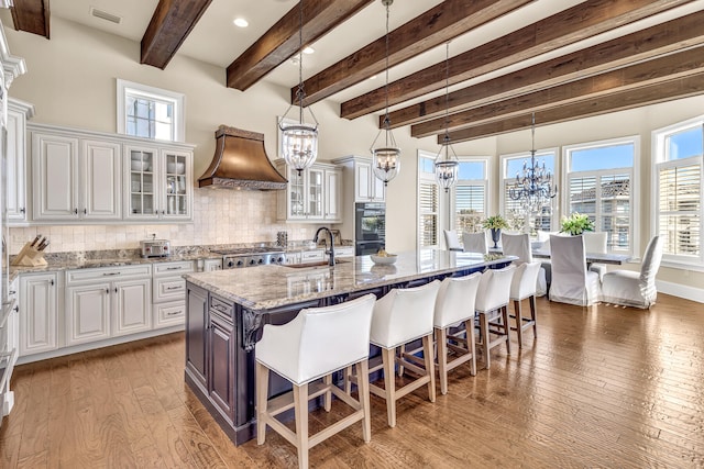 24 Norriego Rd, Destin, FL 32541 - kitchen with premium range hood, light stone countertops, white cabinetry, hardwood / wood-style flooring, and tasteful backsplash