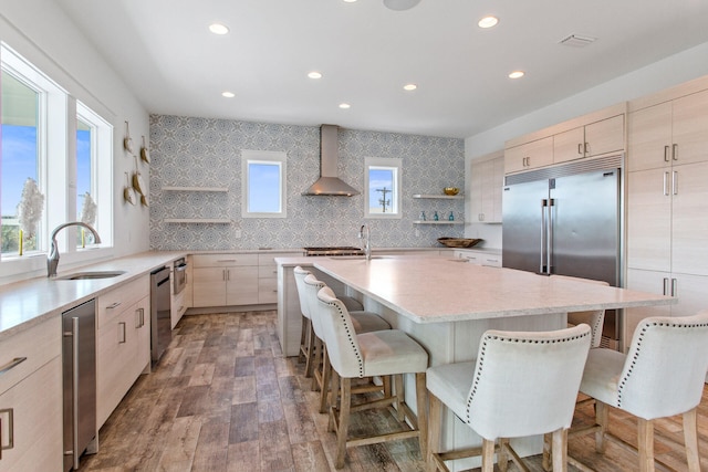 kitchen with wall chimney exhaust hood, sink, a breakfast bar area, dark hardwood / wood-style flooring, and a kitchen island with sink