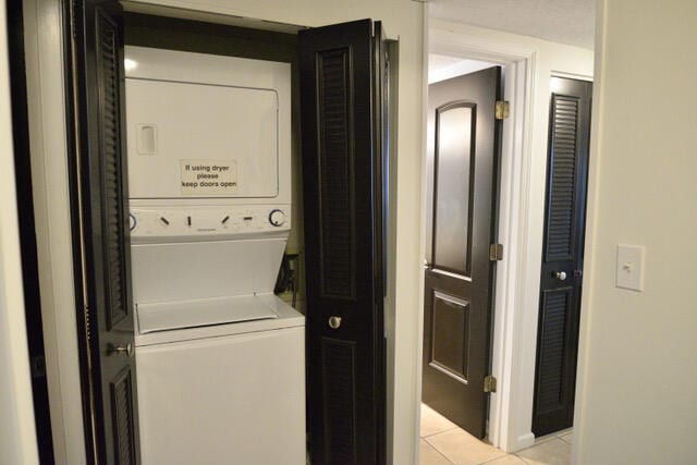 laundry room featuring light tile flooring and stacked washer / drying machine