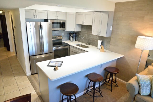 kitchen with a kitchen breakfast bar, backsplash, appliances with stainless steel finishes, light tile floors, and sink