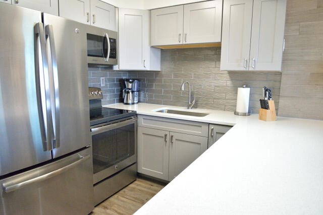 kitchen featuring appliances with stainless steel finishes, light hardwood / wood-style flooring, sink, and tasteful backsplash