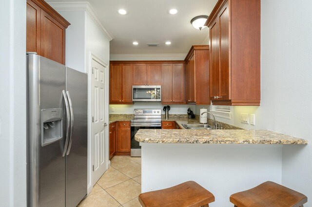 kitchen with light stone countertops, kitchen peninsula, appliances with stainless steel finishes, light tile flooring, and a breakfast bar