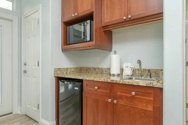 kitchen featuring fridge, light stone countertops, stainless steel microwave, sink, and light hardwood / wood-style floors