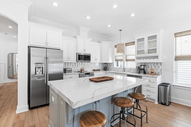 kitchen featuring hanging light fixtures, a kitchen island, high end appliances, tasteful backsplash, and light wood-type flooring