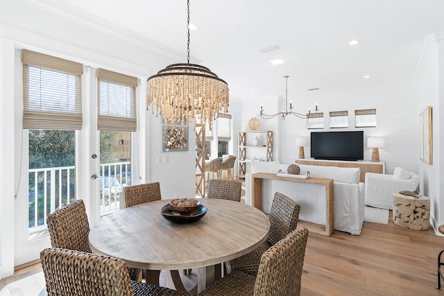 dining space with a healthy amount of sunlight, light hardwood / wood-style floors, an inviting chandelier, and crown molding