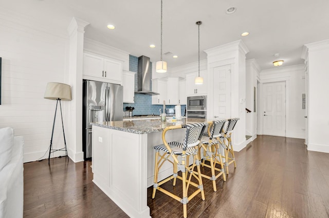 kitchen with a kitchen island with sink, stainless steel appliances, white cabinets, stone countertops, and wall chimney exhaust hood