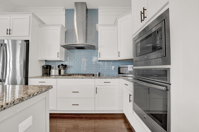 kitchen with white cabinetry, wall chimney range hood, stainless steel appliances, light stone countertops, and backsplash