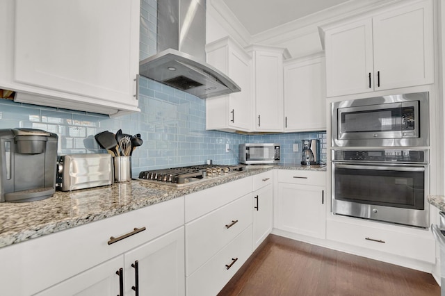 kitchen with crown molding, wall chimney range hood, white cabinets, stainless steel appliances, and backsplash