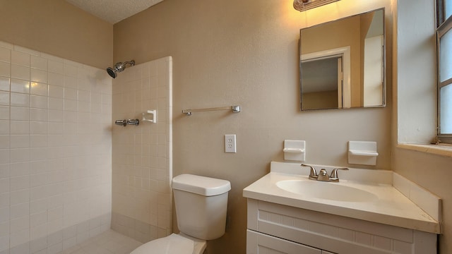 bathroom with vanity, toilet, a textured ceiling, and a tile shower