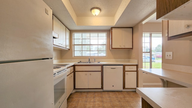 kitchen with sink, a raised ceiling, cream cabinets, a textured ceiling, and white appliances