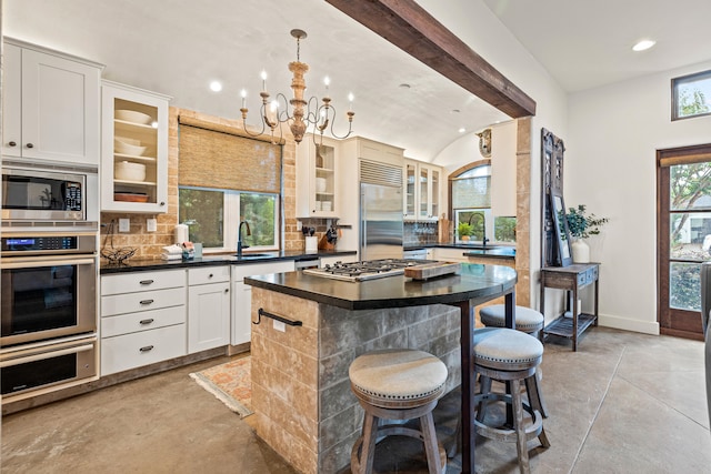 kitchen with built in appliances, backsplash, white cabinetry, pendant lighting, and a chandelier