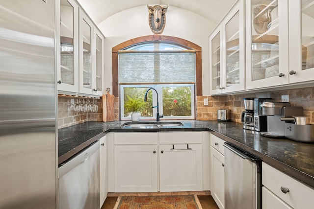 kitchen with white cabinetry, stainless steel appliances, sink, tasteful backsplash, and dark stone counters