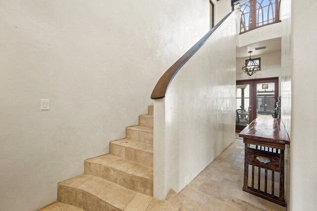 stairs with french doors, a towering ceiling, light tile floors, and a notable chandelier