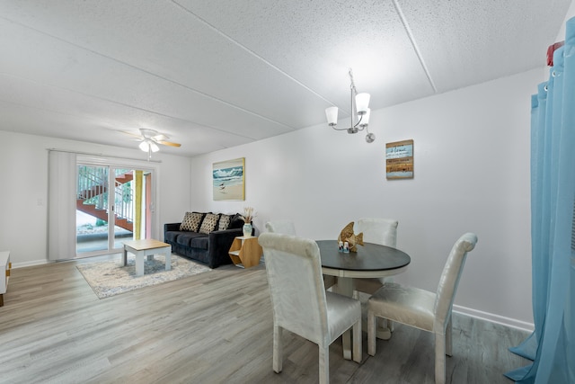 dining room featuring ceiling fan with notable chandelier, wood-type flooring, and a textured ceiling