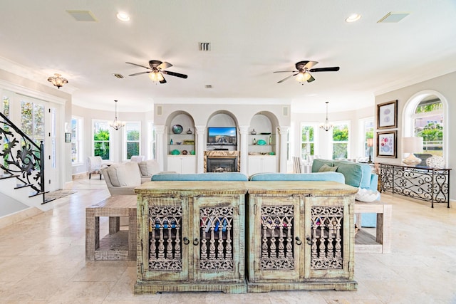 living room with ceiling fan with notable chandelier, built in shelves, and crown molding