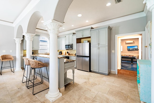 kitchen featuring backsplash, a breakfast bar, ornamental molding, stainless steel appliances, and decorative columns