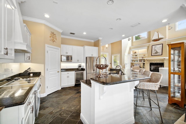 kitchen featuring white cabinets, beverage cooler, a fireplace, appliances with stainless steel finishes, and a kitchen bar