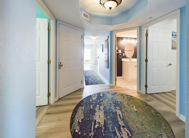 hall with a textured ceiling, light hardwood / wood-style flooring, and sink