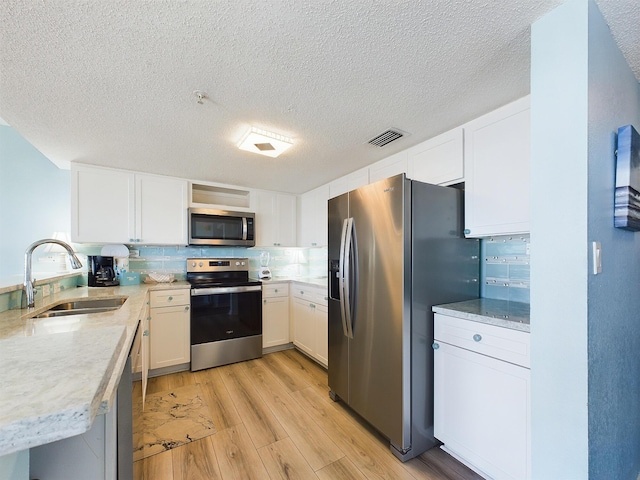 kitchen with white cabinets, sink, light hardwood / wood-style flooring, a textured ceiling, and stainless steel appliances