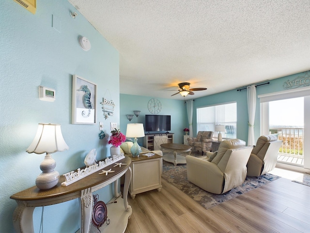 living room with ceiling fan, light hardwood / wood-style flooring, and a textured ceiling