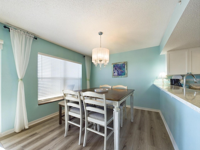 dining room with a notable chandelier, sink, light wood-type flooring, and a textured ceiling