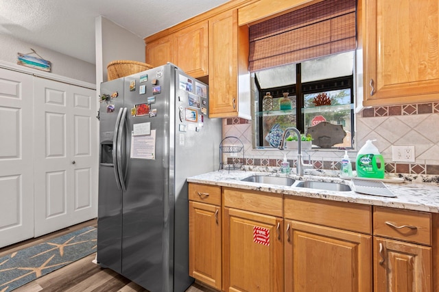 kitchen featuring dark wood-type flooring, backsplash, sink, light stone counters, and stainless steel fridge