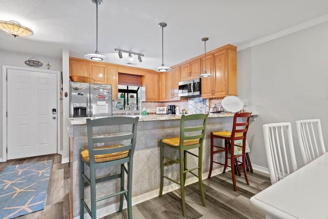 kitchen with hanging light fixtures, stainless steel appliances, dark hardwood / wood-style floors, track lighting, and a kitchen breakfast bar