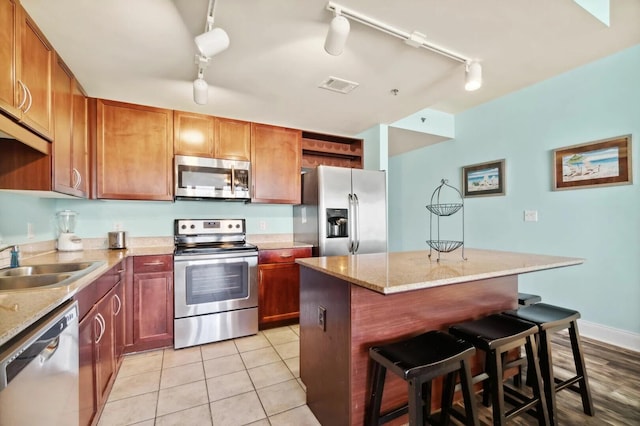 kitchen featuring stainless steel appliances, track lighting, light stone counters, sink, and a center island