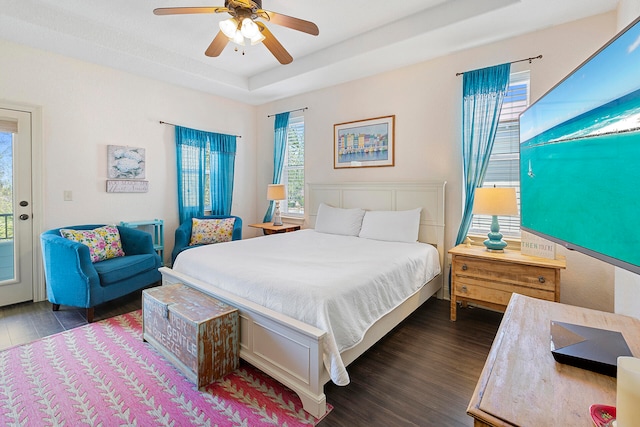 bedroom with dark hardwood / wood-style floors, ceiling fan, a tray ceiling, and access to exterior