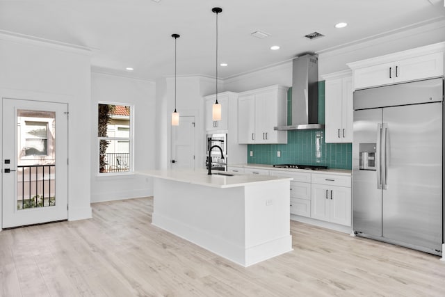 kitchen featuring a kitchen island with sink, white cabinets, light wood-type flooring, wall chimney range hood, and built in fridge