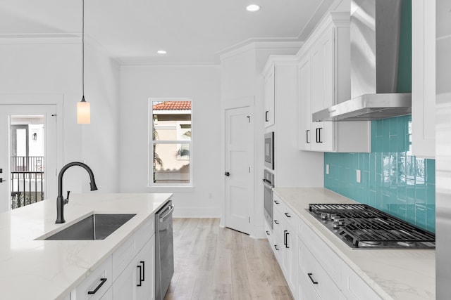 kitchen featuring appliances with stainless steel finishes, hanging light fixtures, tasteful backsplash, wall chimney range hood, and light wood-type flooring