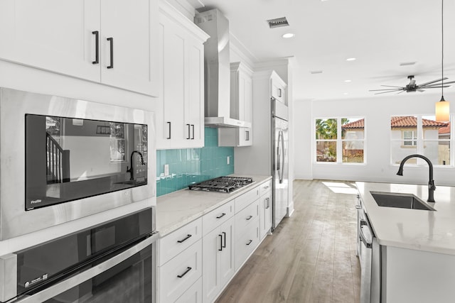 kitchen featuring appliances with stainless steel finishes, ceiling fan, sink, wall chimney range hood, and white cabinetry