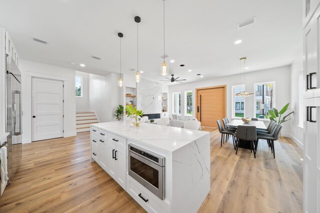 kitchen featuring stainless steel microwave, decorative light fixtures, ceiling fan, and white cabinets