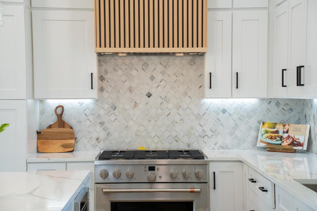 kitchen featuring custom range hood, light stone counters, tasteful backsplash, white cabinets, and high end range