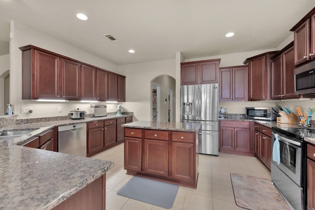 kitchen featuring light tile floors, a kitchen island, sink, stainless steel appliances, and light stone countertops