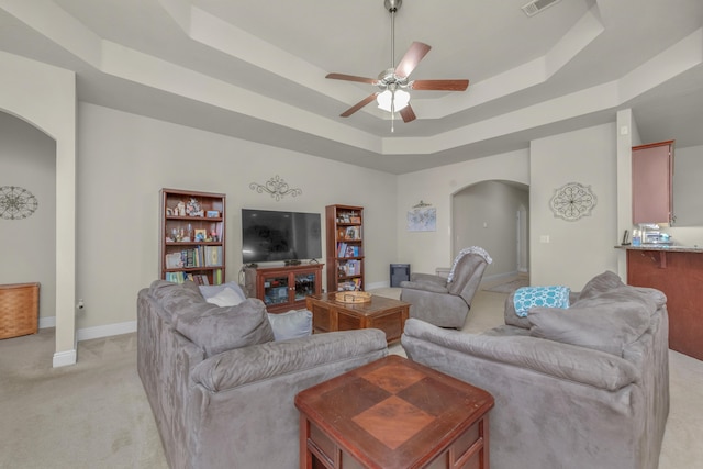 carpeted living room featuring a raised ceiling and ceiling fan