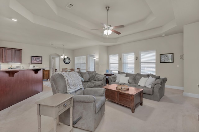 living room with light carpet, ceiling fan with notable chandelier, and a raised ceiling